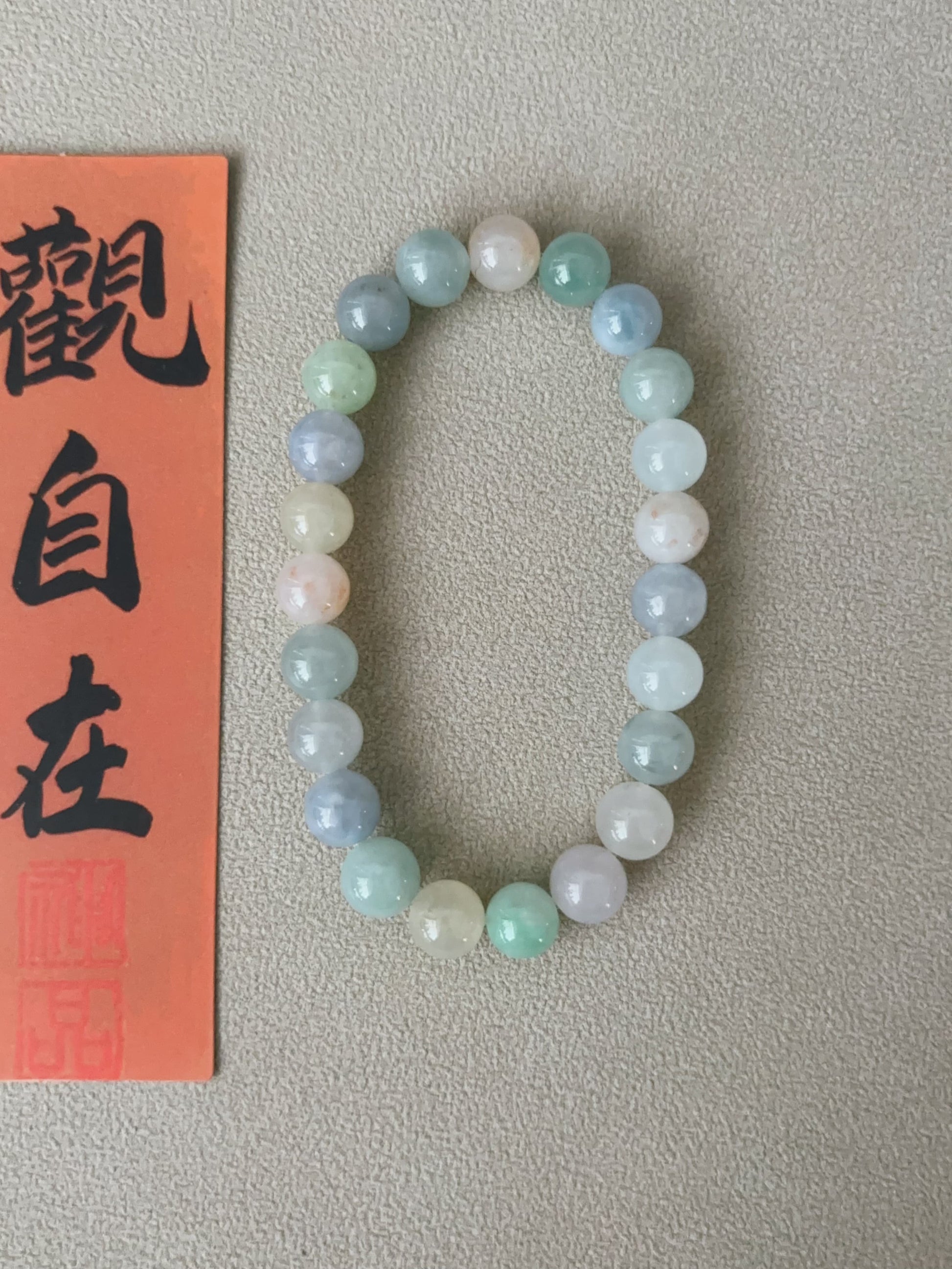 Pastel macaron-colored jade bead bracelet with calligraphy on textured background.